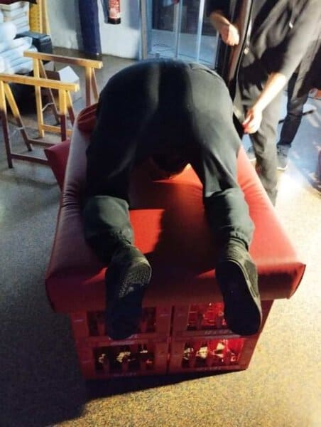Voller K&ouml;rper auf einer roten Kiste liegend, Blick auf den Boden, dunkle Kleidung, indoor, BDSM, Fetisch.