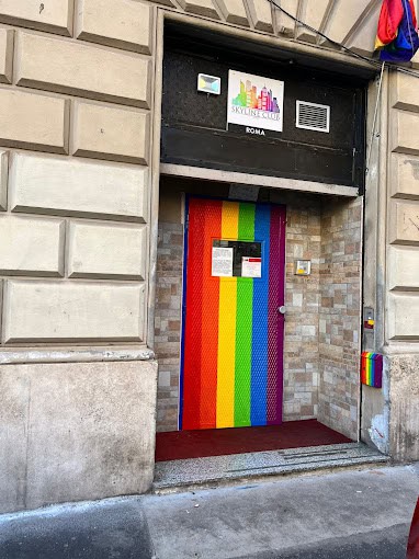 Farbenfrohe LGBTQ+ Flagge am Eingang eines Clubs in Rom, betont Vielfalt und Akzeptanz.