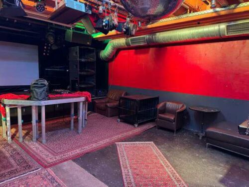 Ein cooler Clubraum mit roten W&auml;nden, Teppichen und chilligen Sitzgelegenheiten f&uuml;r Fisting und Fetisch.