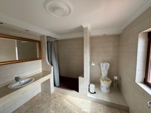 Badezimmer mit Dusche, WC und großem Fenster, helle Fliesen, moderner Stil, natürliche Beleuchtung, sauber und gepflegt, ruhige Atmosphäre, funktionale Einrichtung, komfortabler Raum, freundliche Umge.