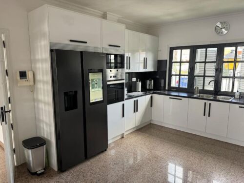 Hochwertige moderne Küche mit schwarzen und weißen Schränken, Kühlschrank, Mikrowelle und großem Fenster für viel Tageslicht.