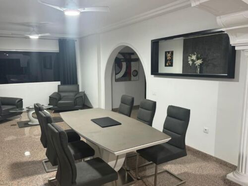 Moderner Konferenzraum mit großem Tisch und schwarzen Stühlen, elegantes Design, weiße Wände, dekorative Wandkunst und eine große Wandspiegelung, ideal für Meetings und Besprechungen.