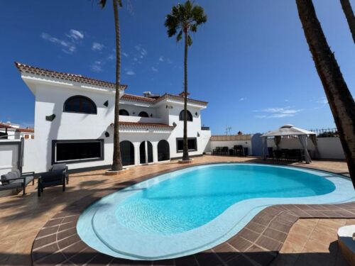 Luxuriöses Ferienhaus mit Pool, weiße Fassade, Palmen, sonniger Himmel, ideal für Erholung und Entspannung in sonniger Umgebung.