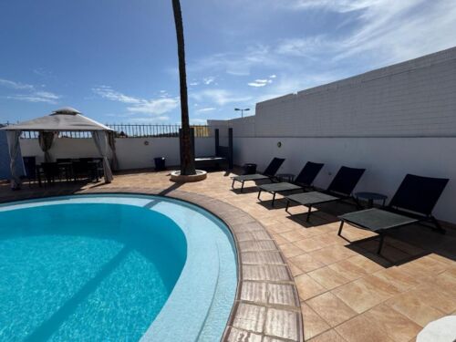 Pool auf einer Dachterrasse mit Sonnenliegen und Sonnenschirm, blauer Himmel und Wolken im Hintergrund, entspannte Atmosphäre, ideal für Erholung und Sonnenbaden.