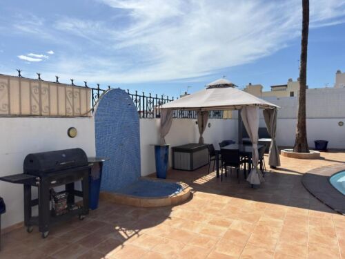 Außenbereich mit Wasserfall, Grill, Sonnenschirm und Pool auf einer Dachterrasse, ideal für Entspannung und Freizeit im Freien.