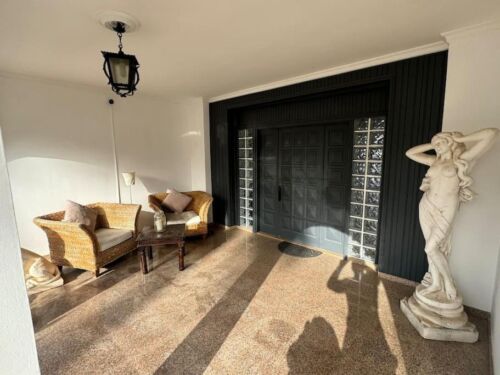 Moderner Eingangsbereich mit schwarzen Garagentor, antiker Skulptur und gemütlicher Sitzecke im Wohnzimmer, natürliche Lichtverhältnisse, stilvolle Inneneinrichtung, elegante Atmosphäre.