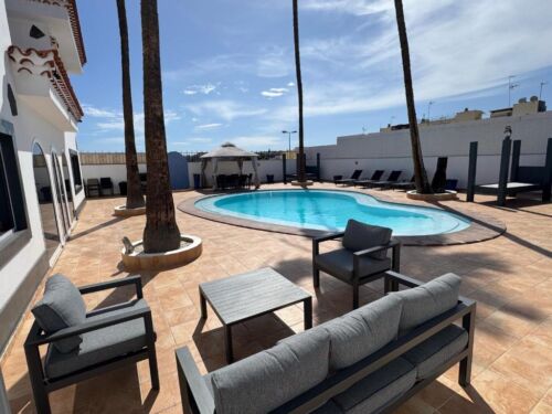 Poolbereich auf einer Dachterrasse mit Sitzgelegenheiten, Palmen und Blick auf den Himmel, ideal für Entspannung und Freizeit in einer warmen, sonnigen Umgebung.