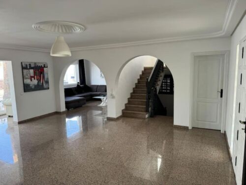 Hochwertiges, modernes Wohnzimmer mit offener Raumgestaltung, eleganten Böden und stilvoller Dekoration, inklusive Treppe und Sitzbereich.