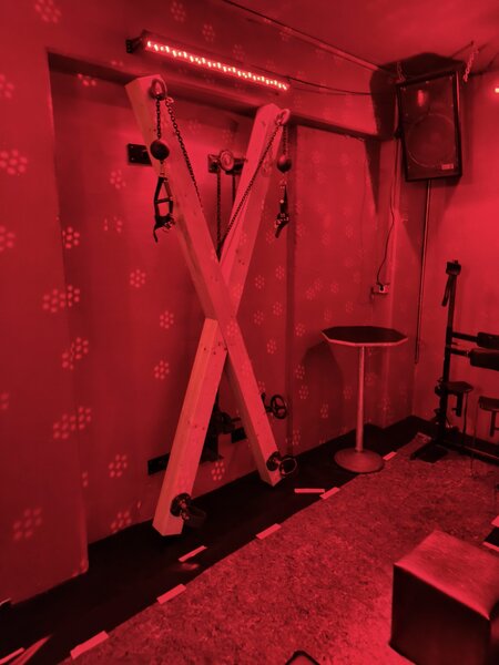 Intimes BDSM Spielzimmer in Stuttgart mit roter Beleuchtung, Holzgestell, Seilen und Zubeh&ouml;r f&uuml;r erotische Spiele und Fetisch-Events.